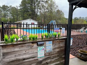 A fenced pool area with a wooden deck, a white building, and a sign indicating no lifeguard on duty. - Cozy Country Oasis (Guyton)
