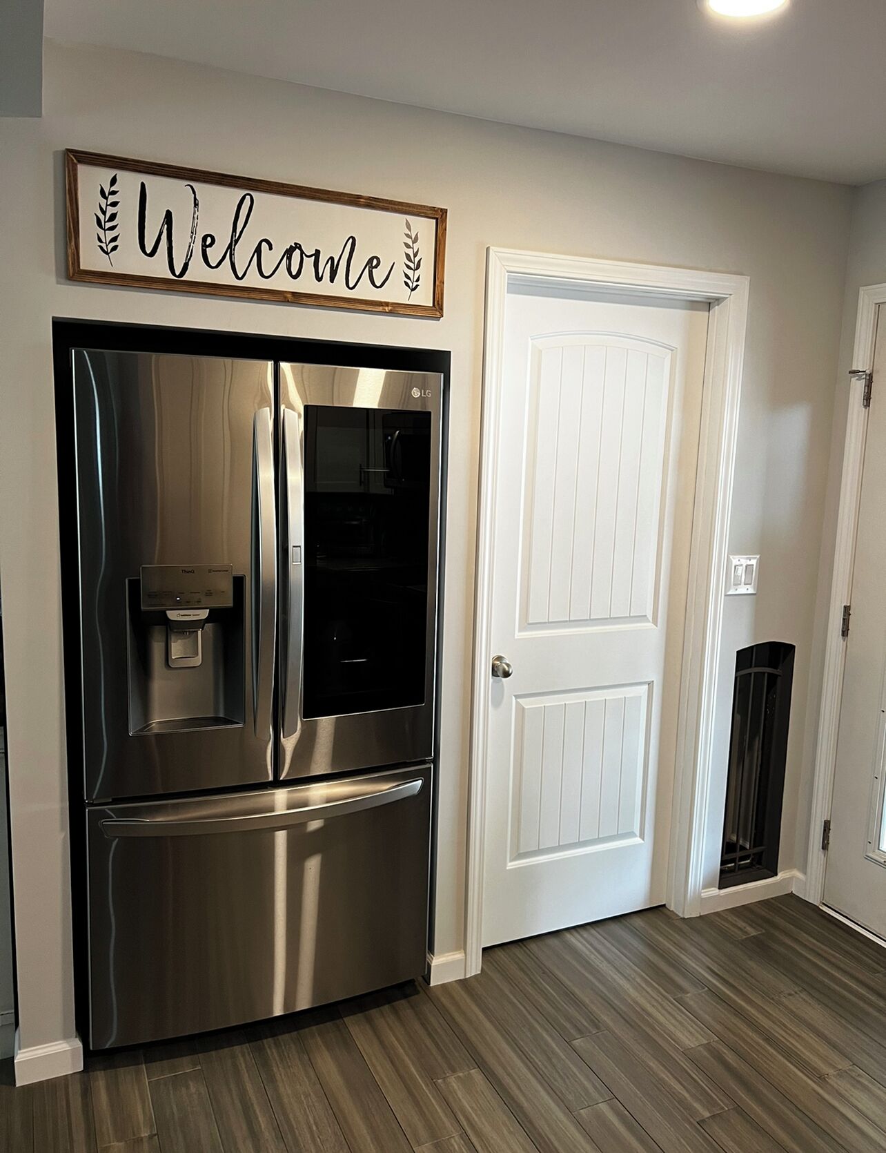 A stainless steel refrigerator with a water dispenser and a 'Welcome' sign above it.