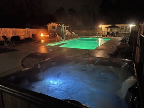 Un jacuzzi con área de piscina iluminada en verde, un espacio de descanso techado y una casa al fondo.