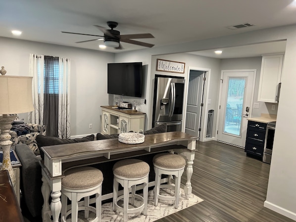 Una cocina moderna con barra, refrigerador, televisor y ventilador de techo.