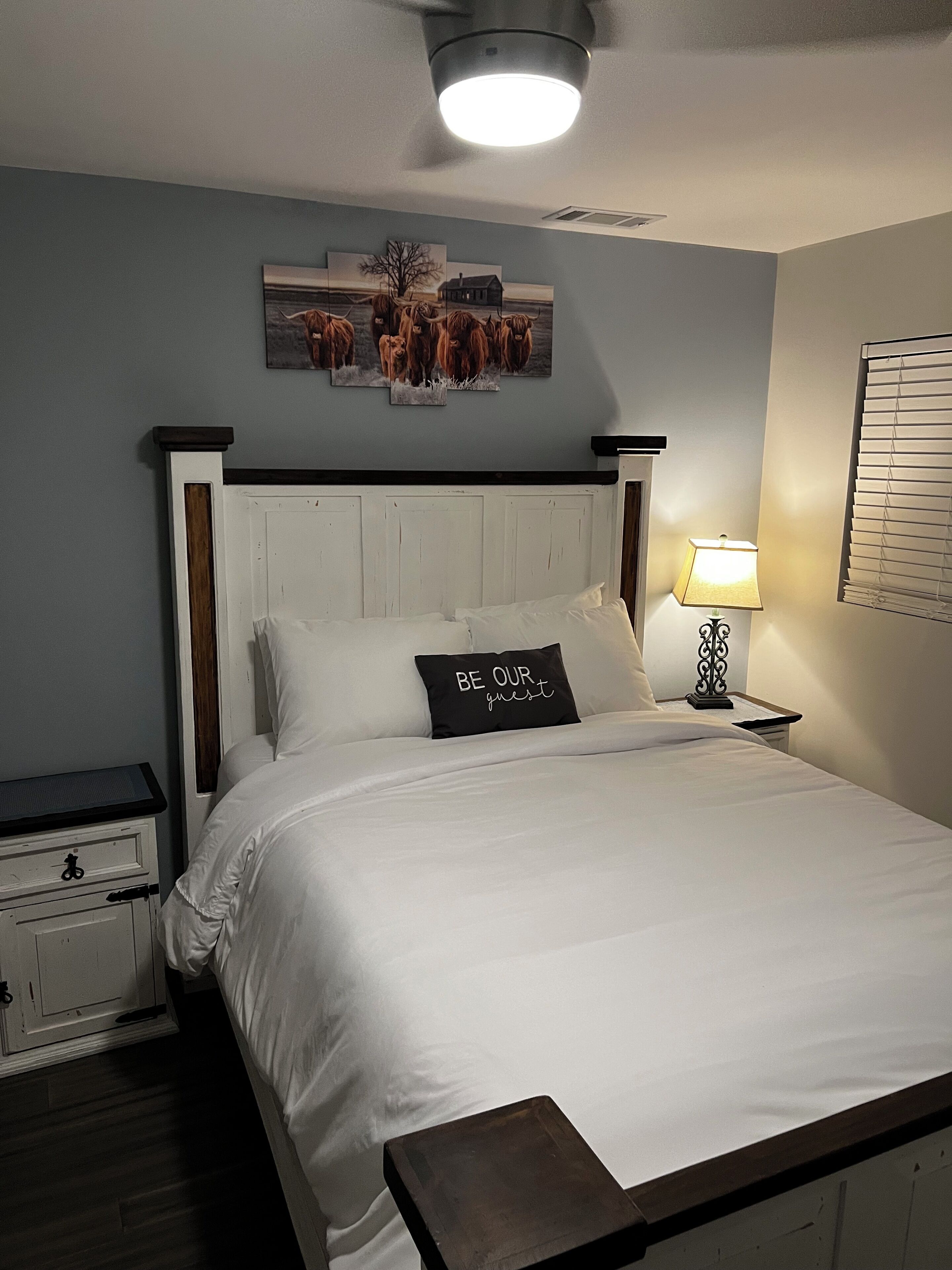 Quarto com cama, mesa de cabeceira, luminária e uma obra de arte pendurada na parede.