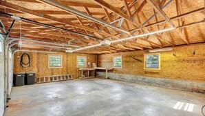 Una stanza spaziosa con pavimento in cemento, pareti in legno e un soffitto alto con travi a vista. Sono presenti due finestre che offrono vista su aree verdi.