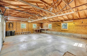 A spacious room with a concrete floor, wooden walls, and a high ceiling with exposed beams. There are two windows with views of greenery outside. - Lazy Dayz - on Lake Keowee with dock, pool, and hot tub (Seneca)