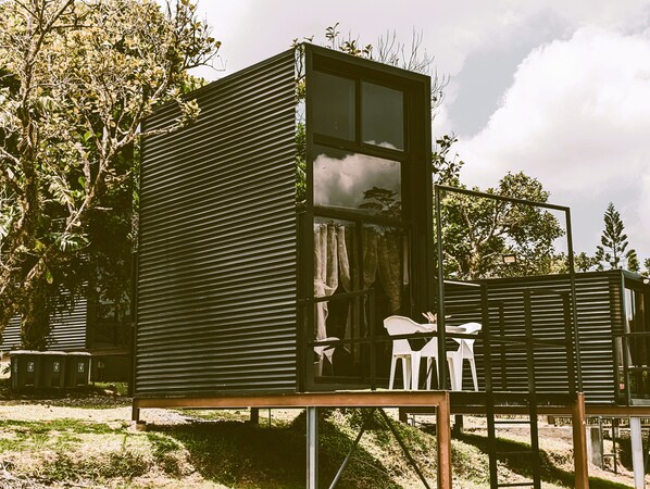 A small, modern cabin with a large window, a door, and a small porch area.