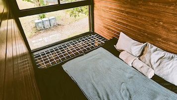 A room with a bed, a window, and a view of greenery outside.