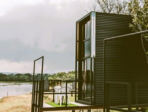 Een modern gebouw met een glazen gevel, uitkijkend op een waterpartij, een terras met stoelen en een vergezicht over het landschap.