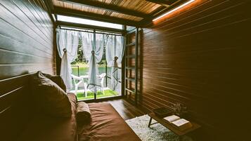 Ein gemütliches Zimmer mit Holzbalkendecke, einer Bank, einem kleinen Tisch mit einem Buch und Blick auf einen Garten durch ein Fenster.