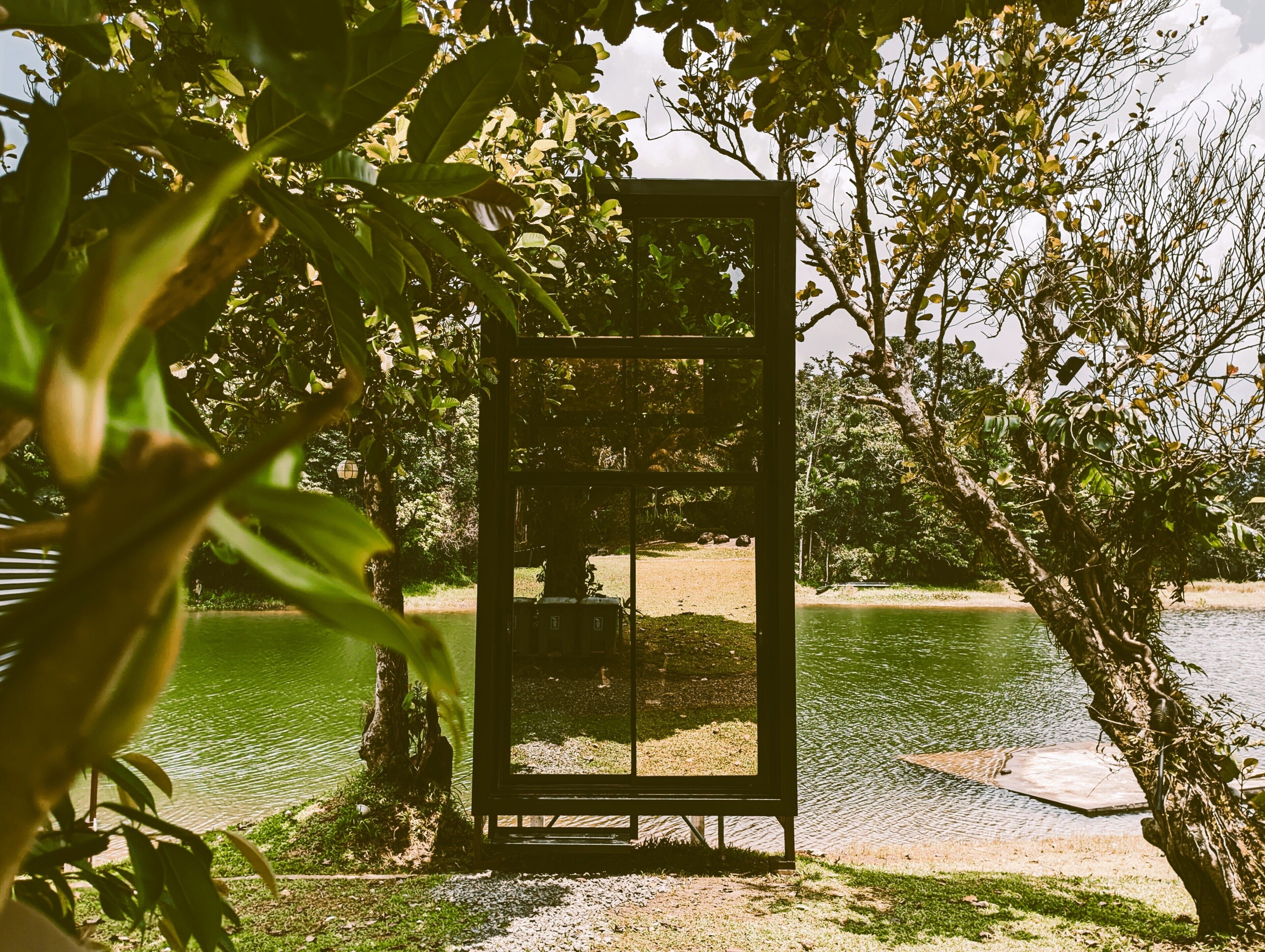 A glass enclosure with a view of a lake and surrounding greenery.