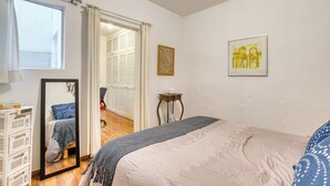 Et soveværelse med en seng, et natbord med lampe, et spejl, et klædeskab og et vindue med gardiner.