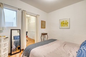 Ein Schlafzimmer mit einem Bett, einem Nachttisch mit Lampe, einem Spiegel, einem Kleiderschrank und einem Fenster mit Vorhängen.