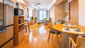 A modern living room with a wooden dining table, chairs, a sofa, and a television. - THE AOCA TOKYO JIYUGAOKA (Setagaya-ku)