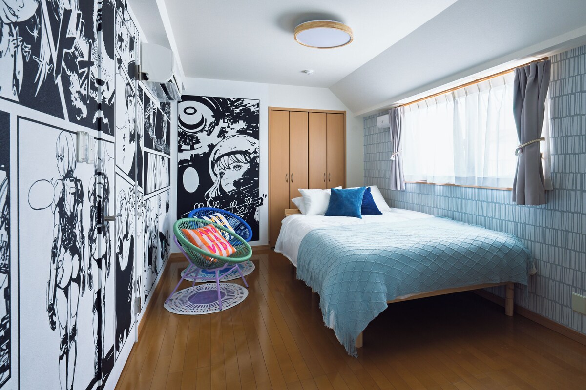 A bedroom with a bed, a wardrobe, a chair, and a wall with comic-style artwork.