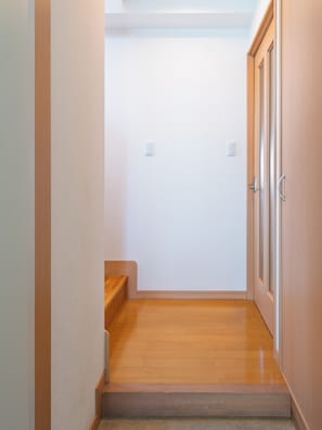 A narrow hallway with a wooden floor, a door on the right, and a light switch on the wall.