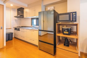 A modern kitchen with a stainless steel refrigerator, a microwave, and a coffee maker on a shelf.