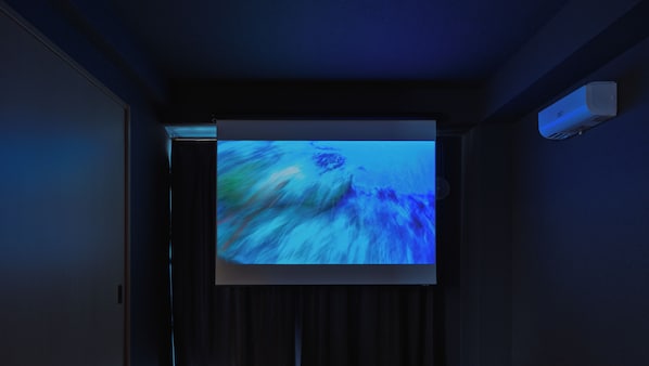 A projection screen displaying a blue abstract image in a dimly lit room with dark curtains and a wall-mounted air conditioning unit.