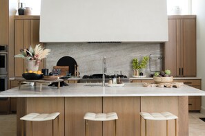 A modern kitchen with a central island, wooden cabinets, a marble countertop, and a built-in stove. - Casa Landing where your soul gets refreshed! A Lakeview custom build with a pool (Carlton Landing)