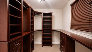 Um closet espaçoso com várias prateleiras e gavetas, um espelho de corpo inteiro e uma janela com persianas.