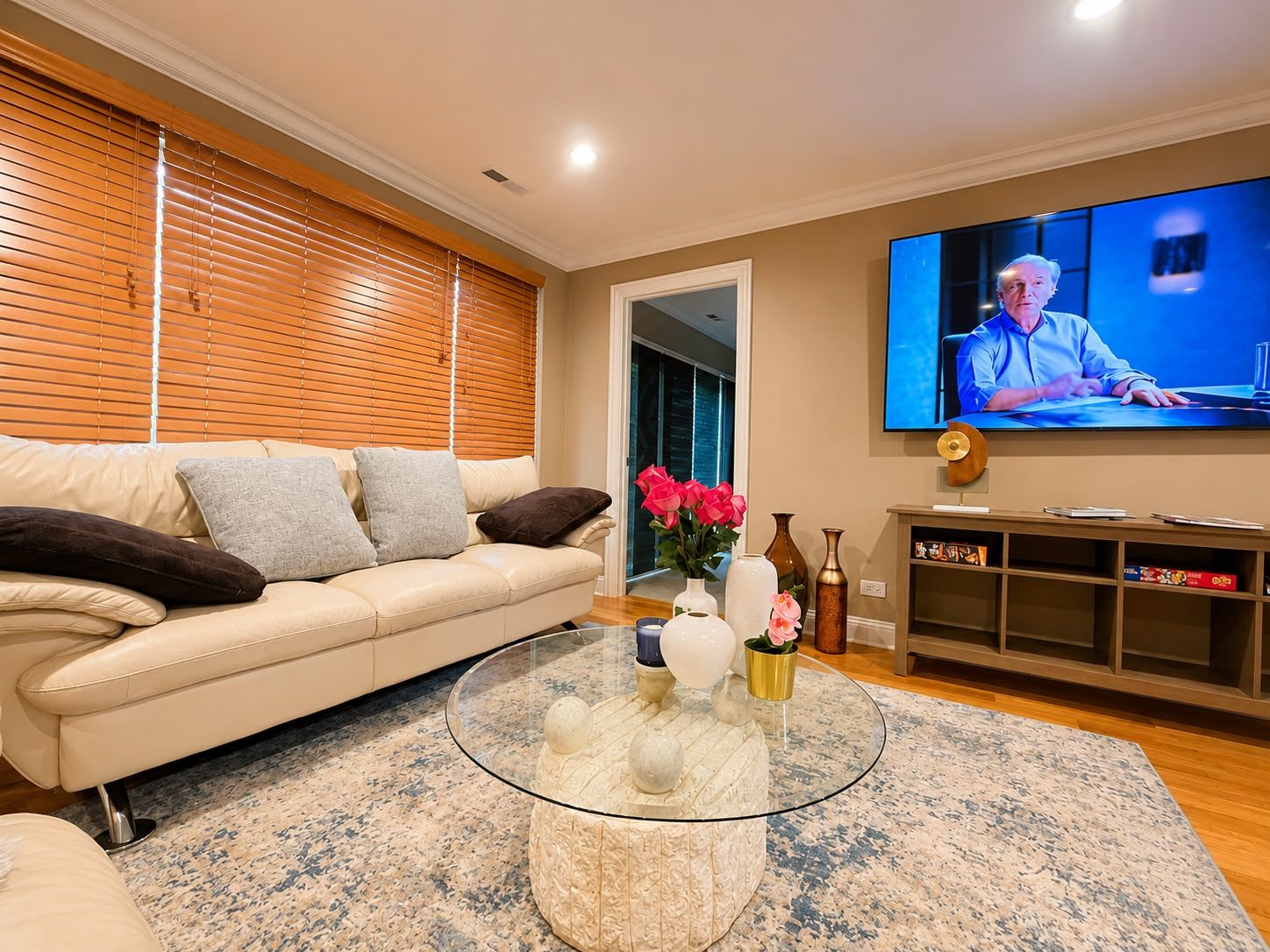 A living room with a beige sofa, a glass coffee table with decorative items, a flat-screen TV, and a wooden cabinet.