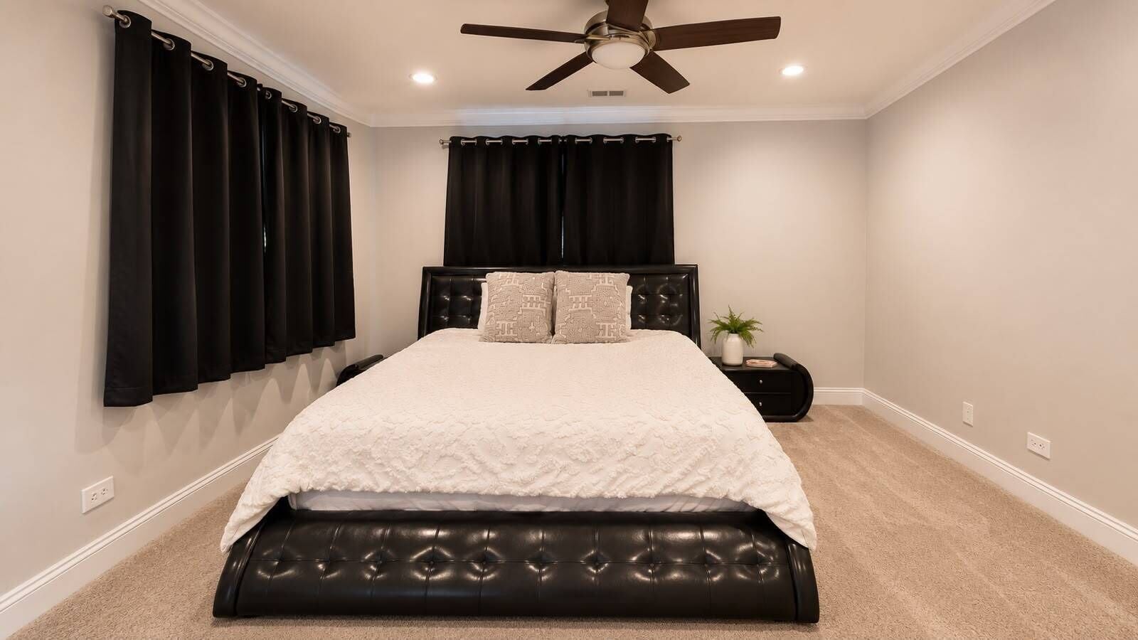 A bedroom with a bed, a ceiling fan, a nightstand, and a window with curtains.