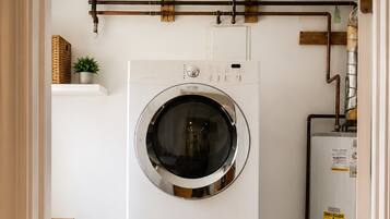 A laundry room with two stacked front-loading washing machines, a water heater, and a wooden floor.