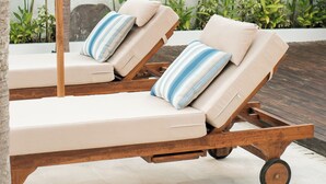 Two lounge chairs with striped cushions, a wooden umbrella, and a backdrop of green plants. - Villa Lurline (Kuta Selatan)