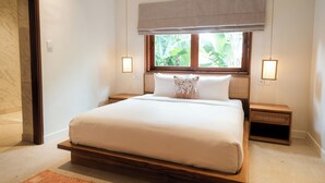A bedroom with a large bed, wooden headboard, two bedside tables, a window with a view of greenery, and a light fixture on each wall. - Villa Lurline (Kuta Selatan)