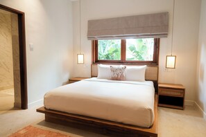 Ein Schlafzimmer mit einem großen Bett, einem Holzkopfteil, zwei Nachttischen, einem Fenster mit Blick auf Grünflächen und einer Leuchte an jeder Wand.