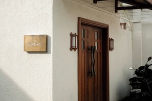 A wooden door with a unique design, a sign with the word 'lounge' on the wall, and a motorcycle parked outside. - Villa Lurline (Kuta Selatan)