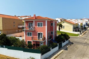 A row of colorful houses with balconies, a clear sky, and a street in the foreground. - Detached Beach House near Santa Cruz | Surf, Yoga & Ocean Views | Sleeps 8–10⁠ (Silveira)