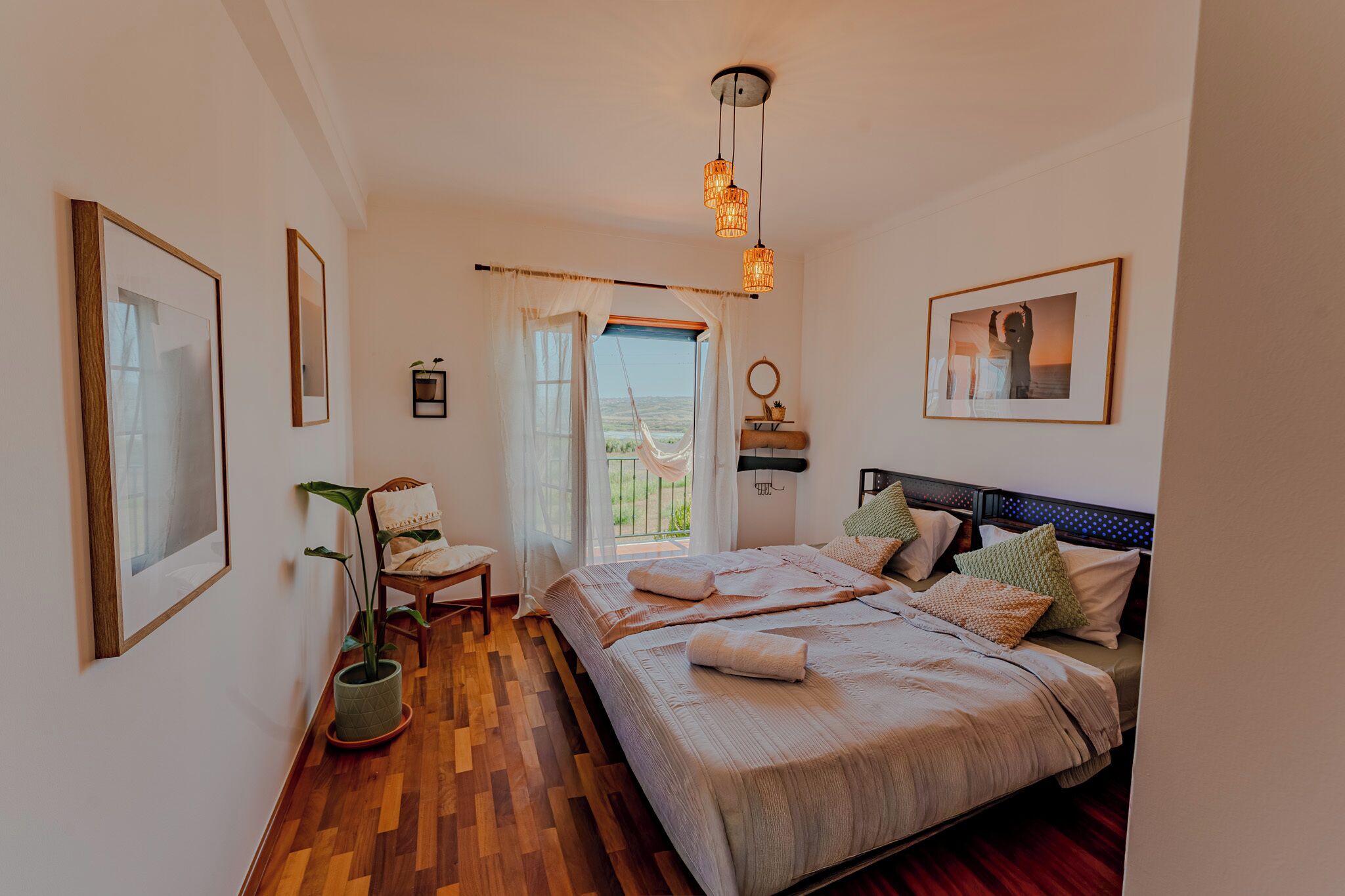 A bedroom with a bed, a chair, a potted plant, and a view of the outdoors.