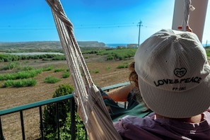 A person sitting on a hammock with a view of a coastal landscape. - Detached Beach House near Santa Cruz | Surf, Yoga & Ocean Views | Sleeps 8–10⁠ (Silveira)