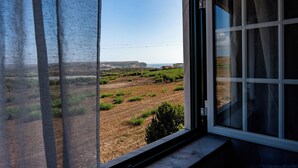 Una stanza con un'ampia finestra che si affaccia su un paesaggio verde e una costa distante.