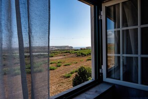 A room with a large window offering a view of a landscape with greenery and a distant coastline. - Detached Beach House near Santa Cruz | Surf, Yoga & Ocean Views | Sleeps 8–10⁠ (Silveira)