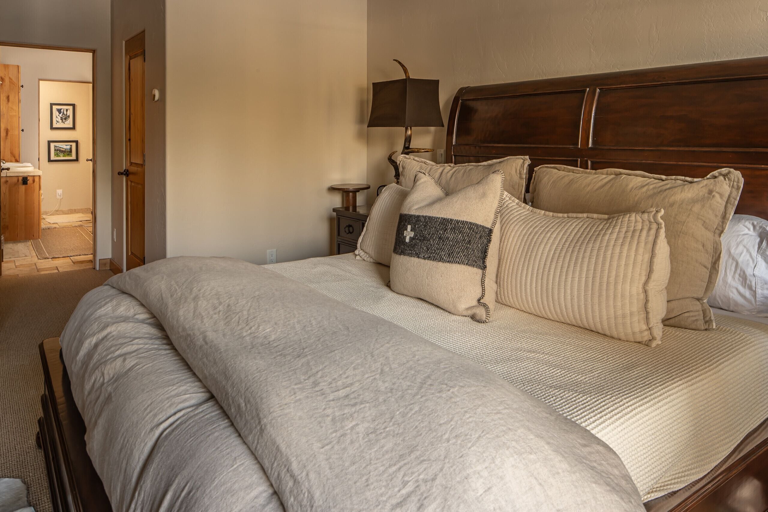 A neatly made bed with a large, textured blanket and several pillows, including one with a cross design.