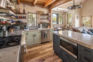 A modern kitchen with a central island, wooden flooring, and a view of the outdoors through large windows. - New Listing! Slopeside at Cowboy Heaven (Big Sky)
