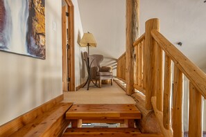 A wooden staircase with a bench at the bottom, a lamp, and a chair in a room with a textured wall and a painting. - New Listing! Slopeside at Cowboy Heaven (Big Sky)