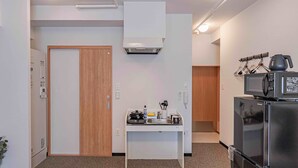 Cocina compacta con microondas, refrigerador y una pequeña encimera con hervidor y utensilios.