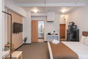 Habitación de hotel con cama, escritorio con computadora, televisor, refrigerador y baño visible a través de una puerta abierta.