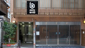 Ingresso di un hotel dal design moderno, caratterizzato da una facciata in listelli di legno verticali e un cartello ben visibile sopra l'ingresso.
