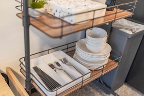 A metal shelf unit with stacked white plates and cutlery, a white pillow with a blue pattern, and a small green plant. - b&Tsutenkaku (Osaka City, Naniwa Ku)