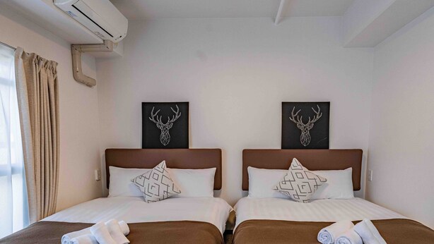 Habitación de hotel con dos camas, cada una con una colcha marrón y almohadas blancas, y dos cuadros de ciervos montados en la pared.