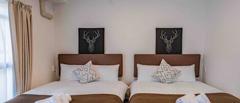 A hotel room with two beds, each with a brown bedspread and white pillows, and two wall-mounted deer head artworks.
