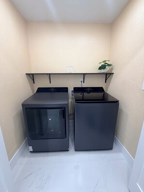 A laundry room with two front-loading washing machines and a shelf above. - Pleasant 3-bedroom house with pool in charming Palm Harbor (Palm Harbor)