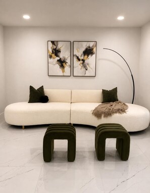 A modern living room with a white sofa, two abstract paintings, a floor lamp, and two green ottomans. - Pleasant 3-bedroom house with pool in charming Palm Harbor (Palm Harbor)