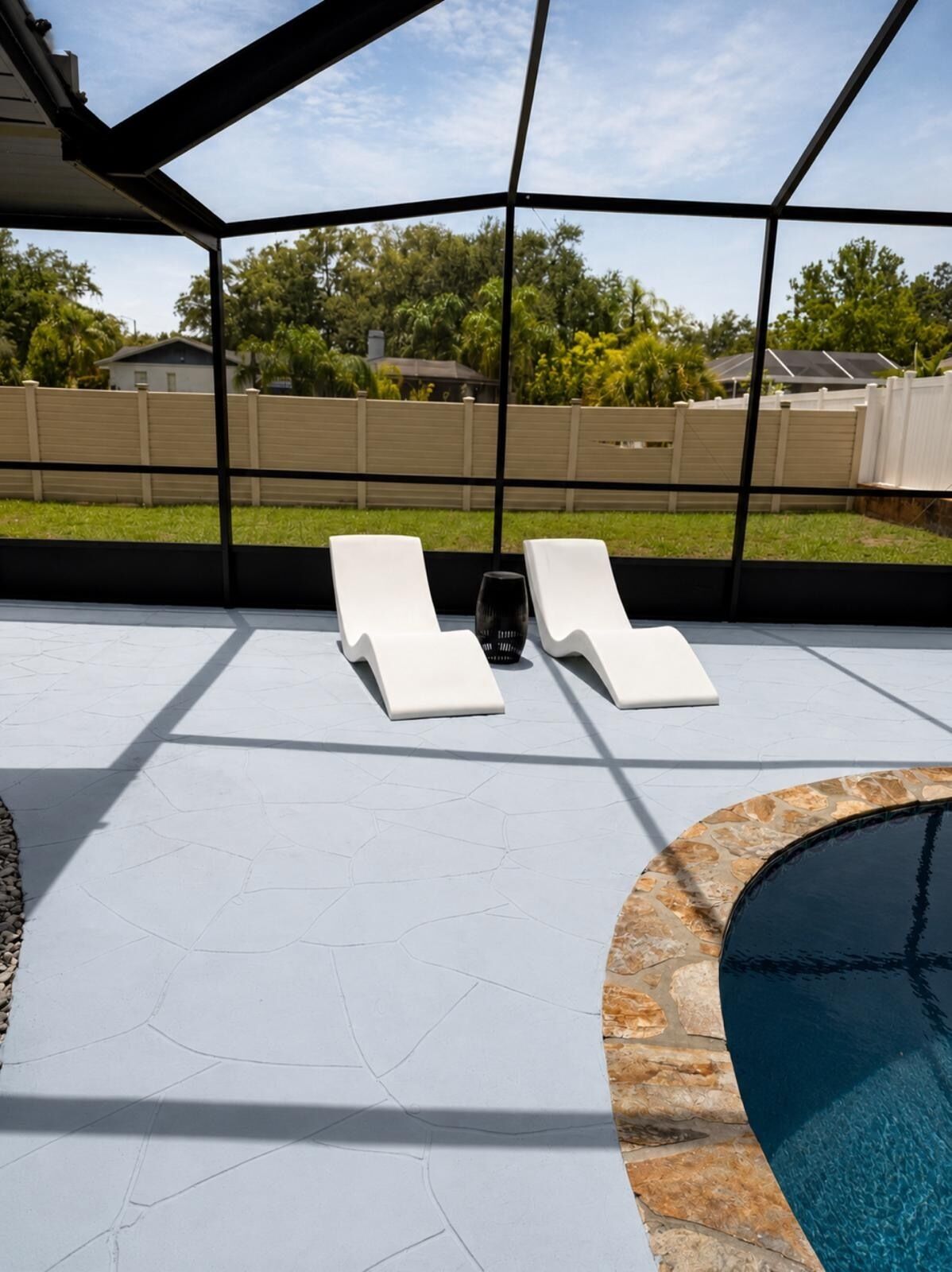 Ein Poolbereich mit zwei Liegestühlen und einem kleinen Tisch, umgeben von einer überdachten Terrasse mit Blick auf einen Garten und einen Pool.