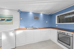 Cuina amb armaris blancs, tauleig de fusta, rentapelats d'acer inoxidable i forn de mur.