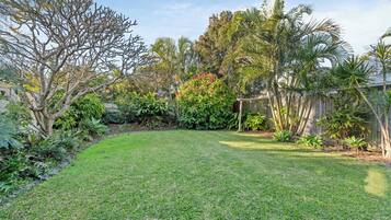 A well-maintained backyard with a grassy lawn, various shrubs, and a wooden fence.