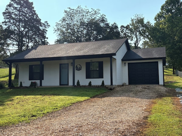 A single-story house with a front porch, a garage, and a gravel driveway.
