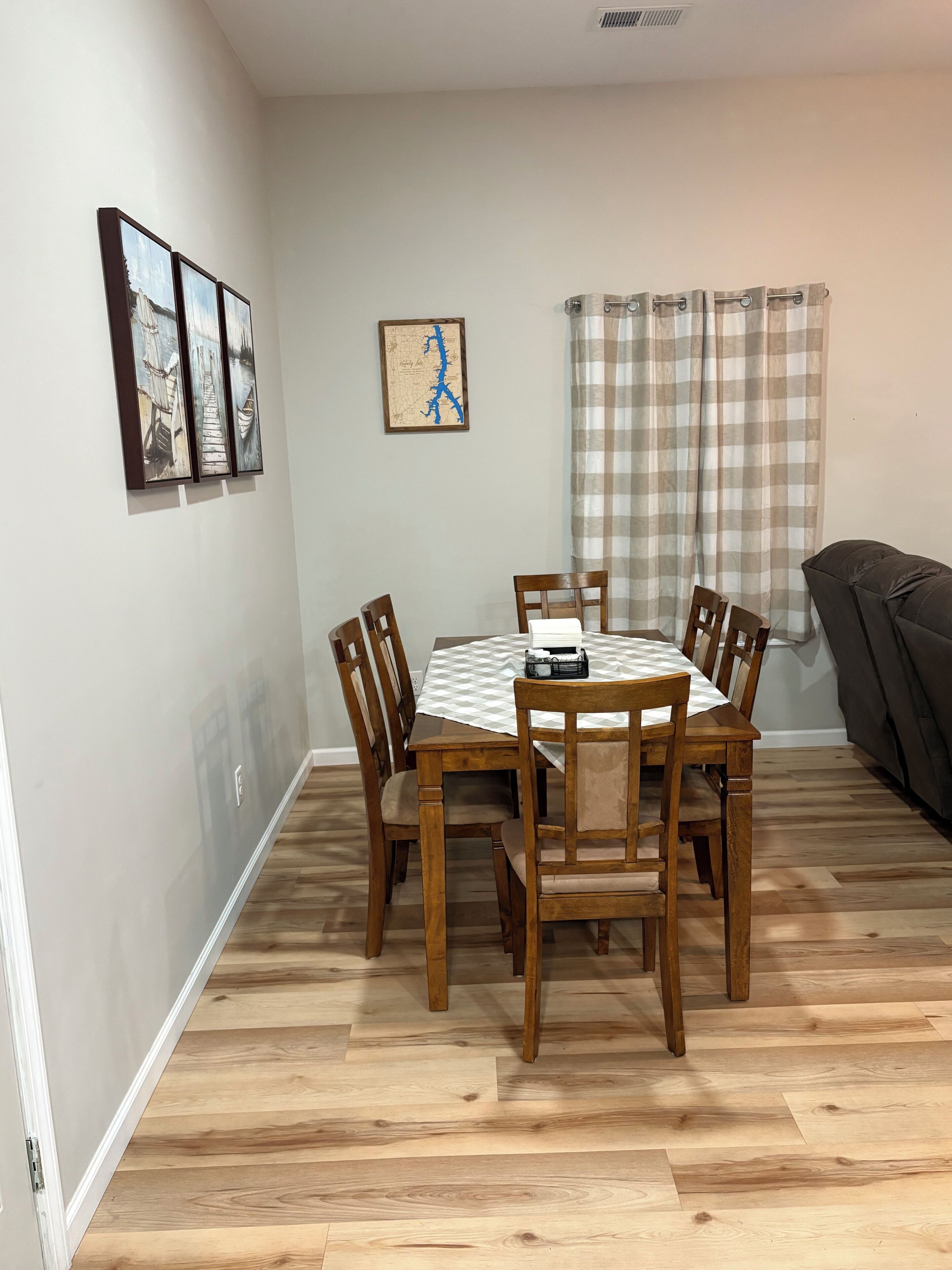 A dining area with a wooden table and chairs, a map on the wall, and a checkered curtain.