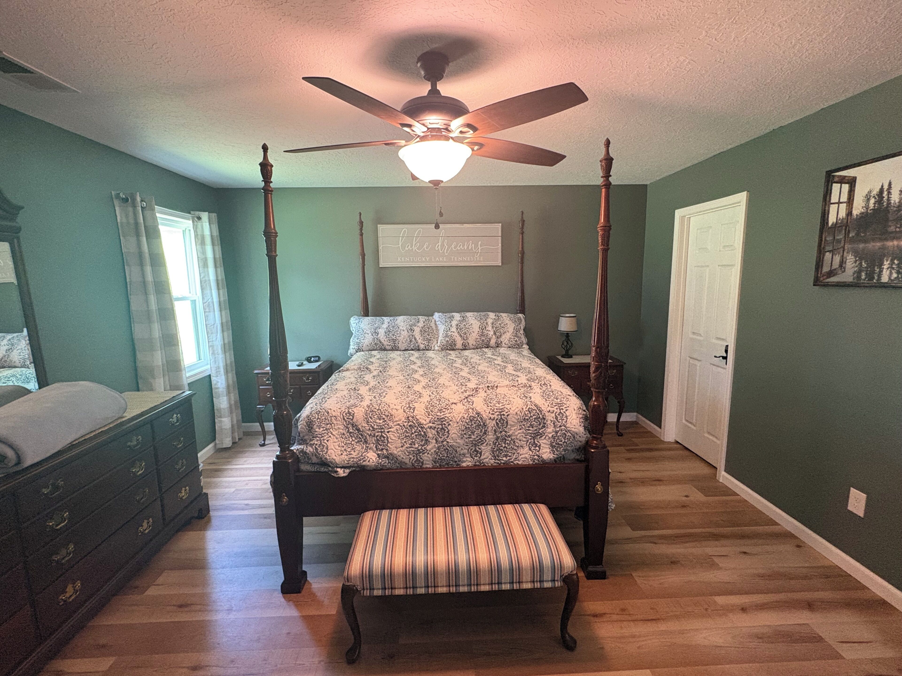 A bedroom with a four-poster bed, a nightstand, a bench, a dresser, and a ceiling fan.